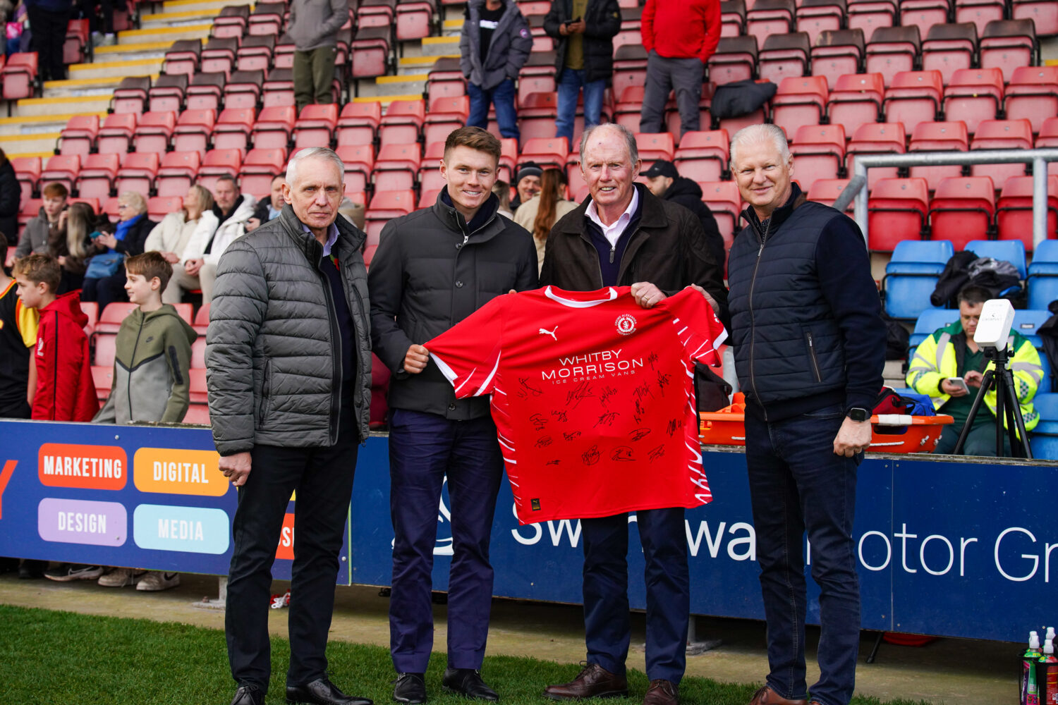 Steve Morgan holding a signed shirt with members of Crewe Alexandra in the Community